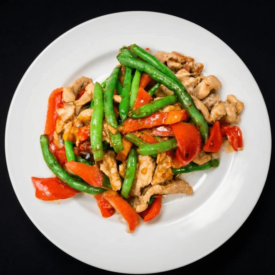 Stir-fried chicken with green beans and red bell peppers on a white plate.