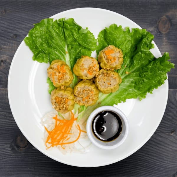 Six steamed dumplings with toppings on lettuce, with shredded carrots, daikon, and a side of soy sauce.