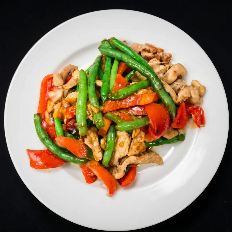 Stir-fried chicken with green beans and red bell peppers on a white plate.