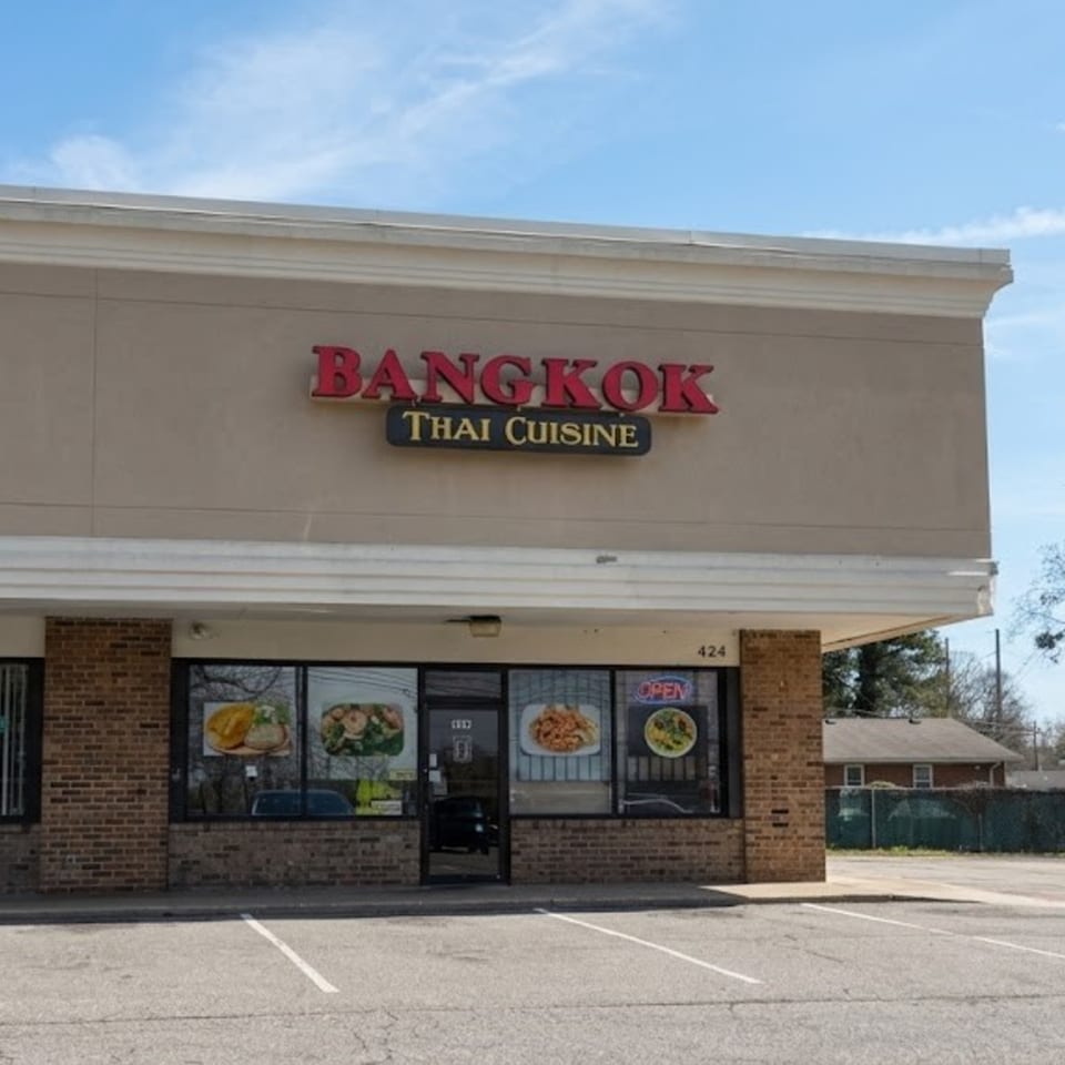 Exterior of Bangkok Thai Cuisine restaurant with a tan facade, red sign, and food posters in windows.