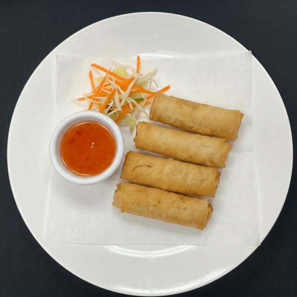 Four golden spring rolls with sweet chili sauce and shredded vegetables on a white plate.